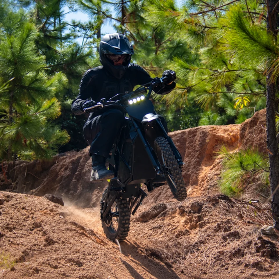 Rider on a high performance electric dirt bike on a wooded dirt trail